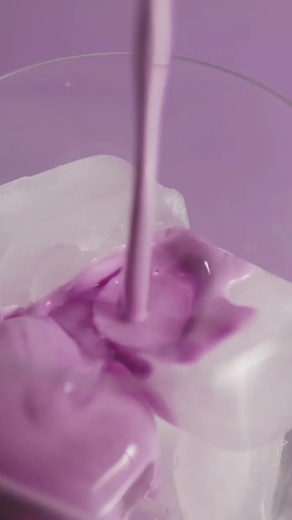 Lavender liquid streaming onto ice cubes inside a clear glass.