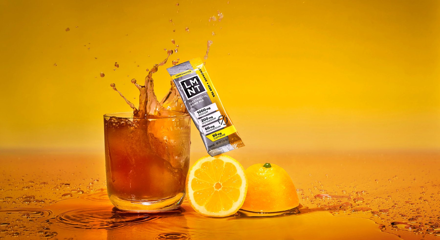 LMNT packet balanced on iced tea glass with splashing liquid and lemons.