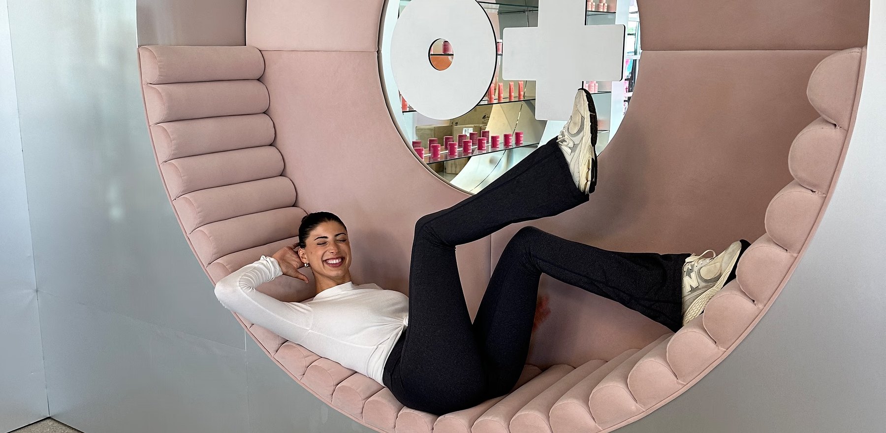 Brianna Bitton laughs while reclining in a pink retail nook.