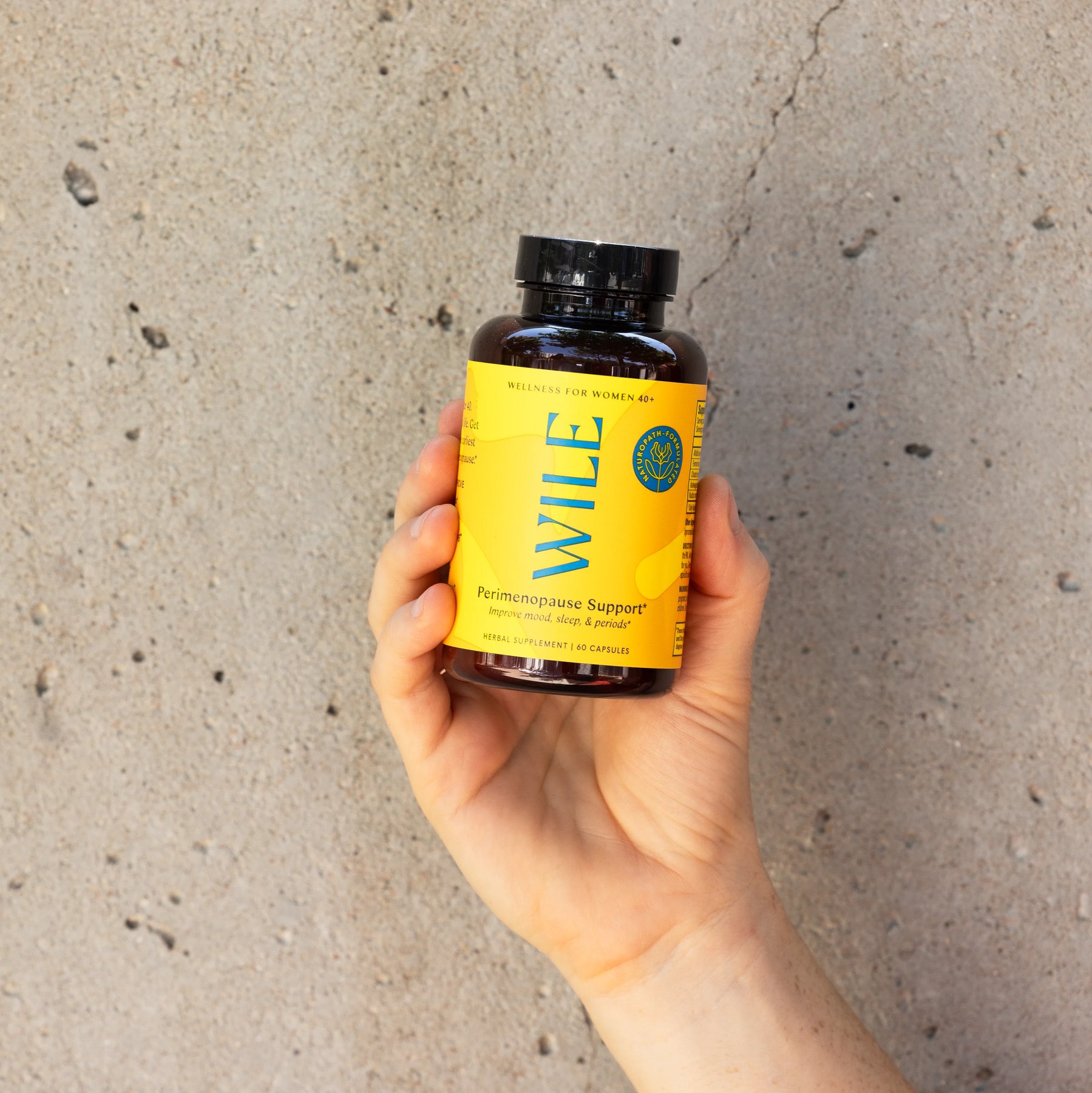 Hand holds yellow Wile Perimenopause Support bottle against concrete.