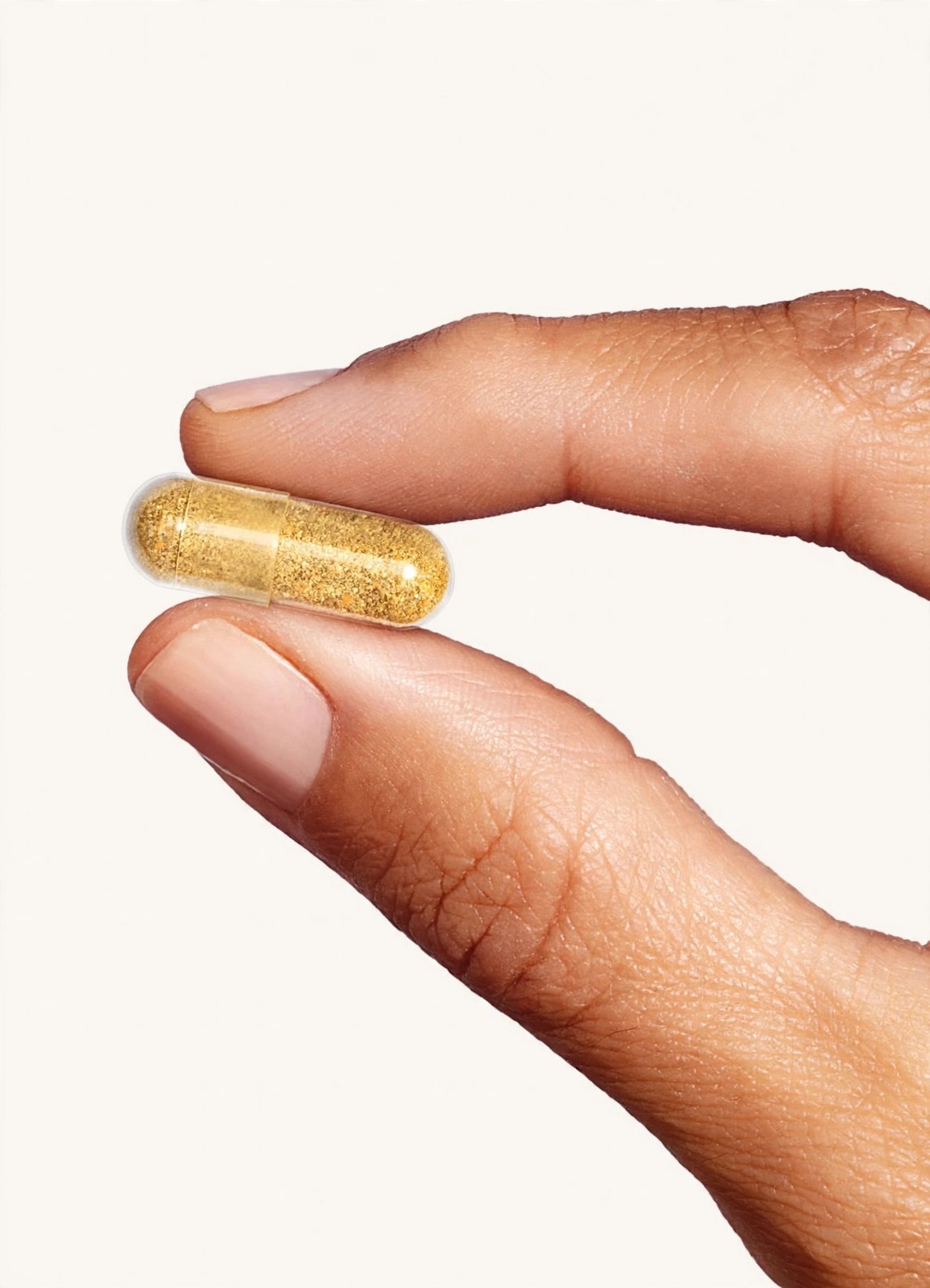Fingers hold a golden supplement capsule against a light background.