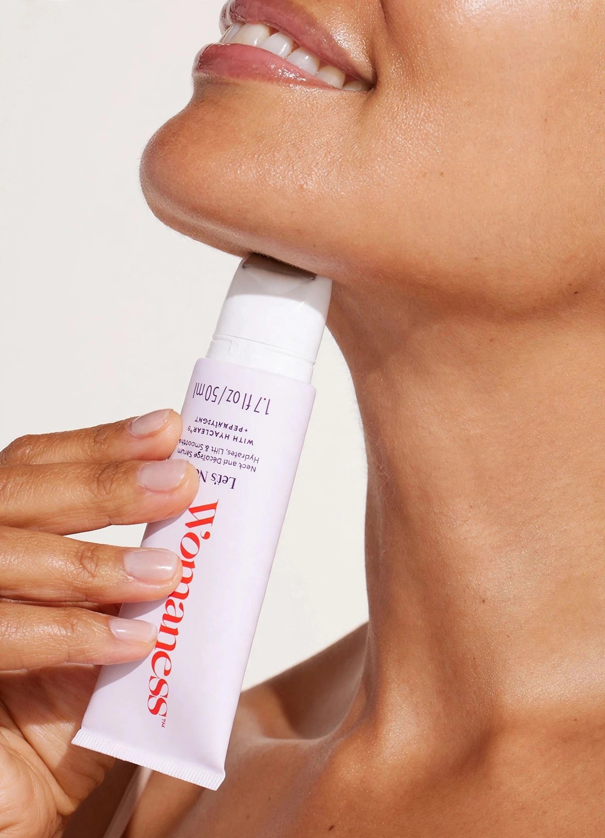A woman applies Womaness serum tube to her neck and chin.